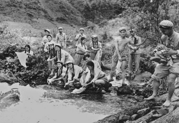 1952年9月，志愿军第12军文工团为迎接祖国慰问团和国庆节演出在朝鲜某地边休整边排练。图为休息时他们在小河边洗衣服。