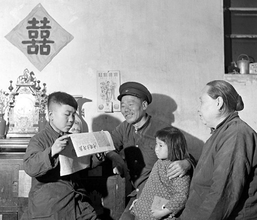 这是1954年5月，北京长辛店机车车辆修理厂老工人佐士俊（左二）在家中听次子读《中国少年报》。 新华社发